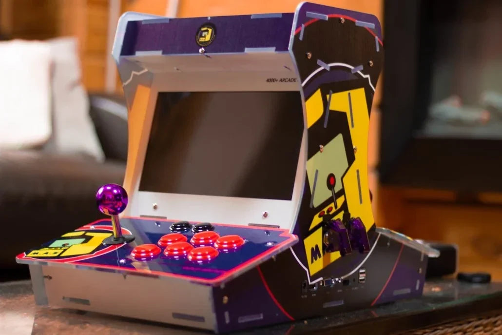 Tabletop mini arcade machine next to a 2Bluebox Retro Game Stick 4K Pro and two 2.4GHz wireless controllers in front of a TV