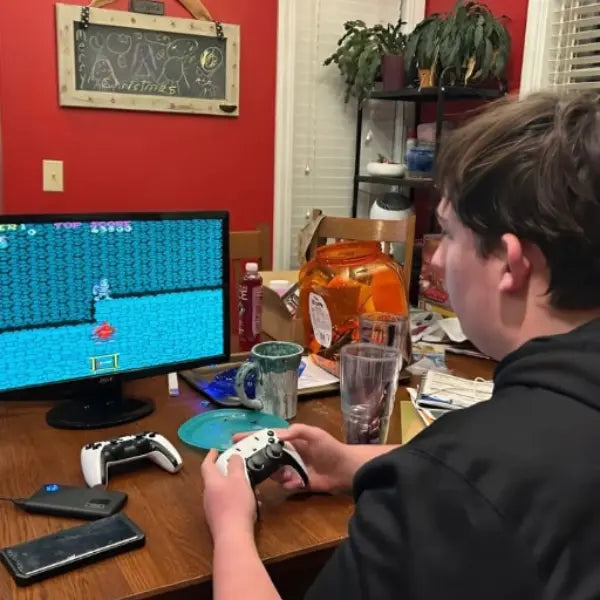 Person playing a retro video game on a computer with 2Bluebox Retro Game Console on the desk.
