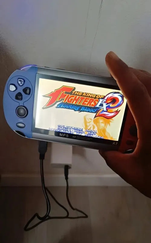 Hand holding X7 handheld console playing King of Fighters EX2 Howling Blood while connected to charger.